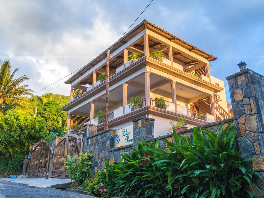 Un edificio a più piani con facciata in pietra, balconi fioriti e un cartello con la scritta "Blue Pearl".