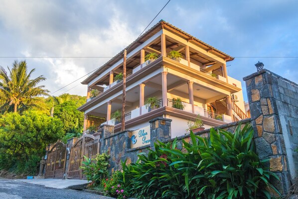 Un edificio de varios pisos con fachada de piedra, balcones con plantas y un letrero que dice "Blue Pearl".