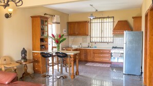 Una cocina con armarios de madera, un refrigerador, un comedor con taburetes y un florero con flores.
