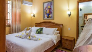 Una cama bien hecha con sábanas blancas y toallas decorativas en forma de cisnes, un cabecero de madera, una mesita de noche pequeña, una lámpara de pared y un cuadro de flores.