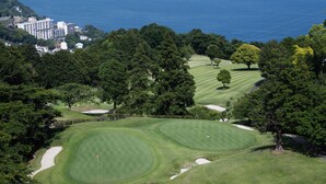 A golf course with sand bunkers, a flag, and a view of the ocean. - Atami Club Geihinkan (Atami)
