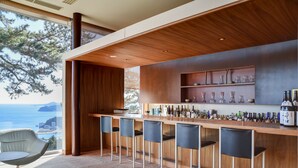 A modern bar area with a wooden counter, bar stools, and a view of the ocean. - Atami Club Geihinkan (Atami)