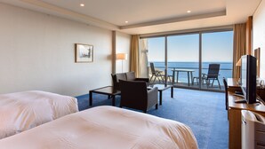 A hotel room with two beds, a desk, a chair, a TV, and a large window with a view of the sea. - Atami Club Geihinkan (Atami)