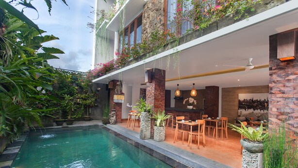 A pool area with a stone border, outdoor seating, and potted plants. - Ning Villa Ubud by GenuineHost (Ubud)