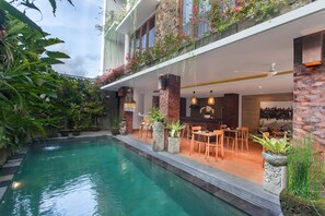 A pool area with a stone border, outdoor seating, and potted plants. - Ning Villa Ubud by GenuineHost (Ubud)
