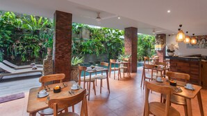 A restaurant with wooden tables and chairs, a pool, and lush greenery. - Ning Villa Ubud by GenuineHost (Ubud)