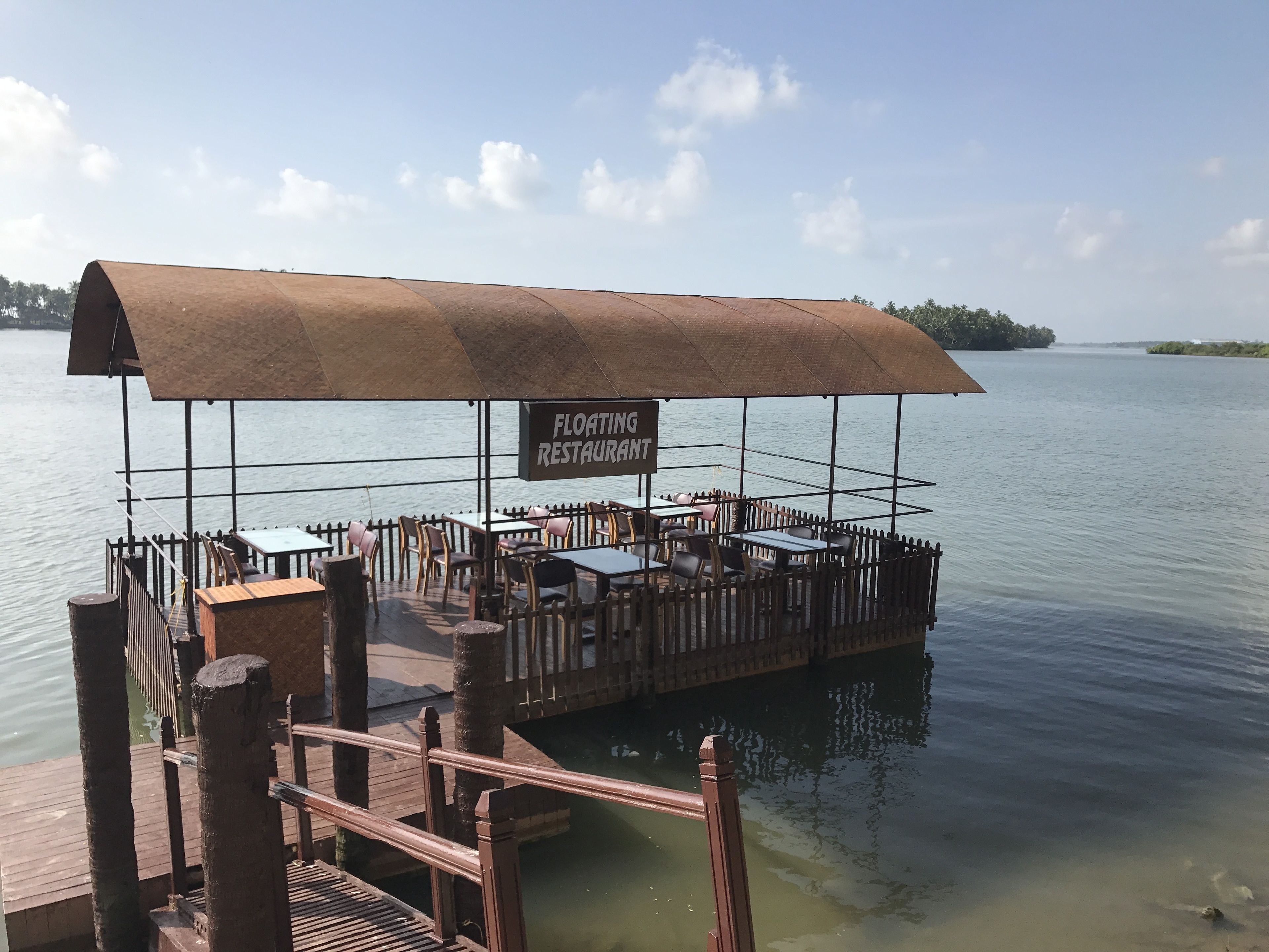 Ein schwimmendes Restaurant mit überdachter Terrasse, Tischen und Stühlen, umgeben von Wasser.