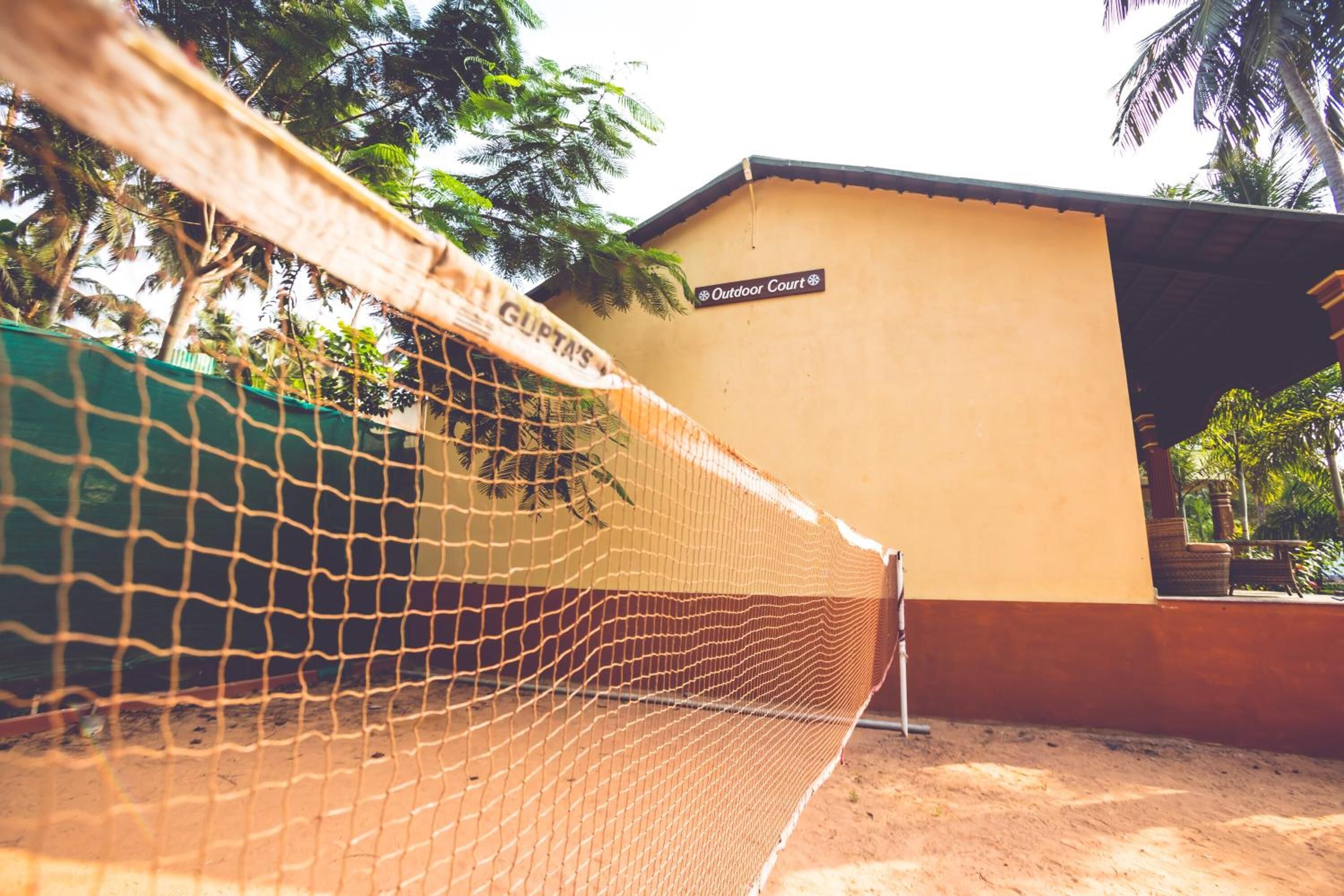 A netted area with a sign reading "Outdoor Court" and a building with a yellow wall and a roof.