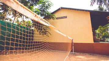 A netted area with a sign reading "Outdoor Court" and a building with a yellow wall and a roof.