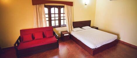 A room with a bed, a red sofa, a nightstand, and a window with curtains.