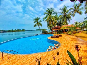 A swimming pool with a wooden deck, surrounded by palm trees and a view of the sea. - Paradise Lagoon (Udupi)