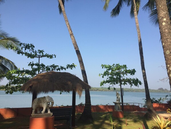 A serene outdoor area with a thatched-roof structure, palm trees, and a statue of an elephant. - Paradise Lagoon (Udupi)