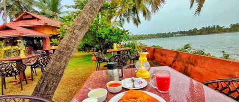 A table with a meal, including a slice of pizza, bowls of sauce, and a drink, set against a backdrop of a beach and palm trees.
