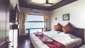 Een hotelkamer met een bed, een plafondventilator, een airconditioningapparaat, een raam met gordijnen en uitzicht op het water.