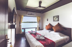 Una habitación de hotel con una cama, ventilador de techo, unidad de aire acondicionado, ventana con cortinas y vista al agua.