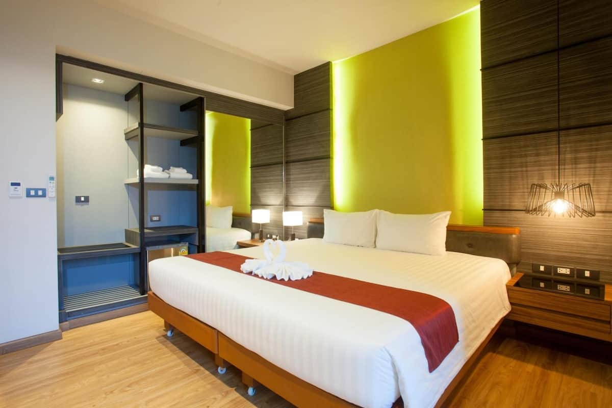 Une chambre d’hôtel moderne dotée d’un grand lit, d’un plancher en bois, d’une armoire intégrée et d’un mur d’accent aux couleurs vives.