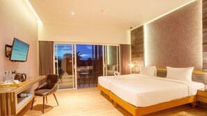A hotel room with a large bed, a desk with a computer, and a view of the outdoors through a sliding door.