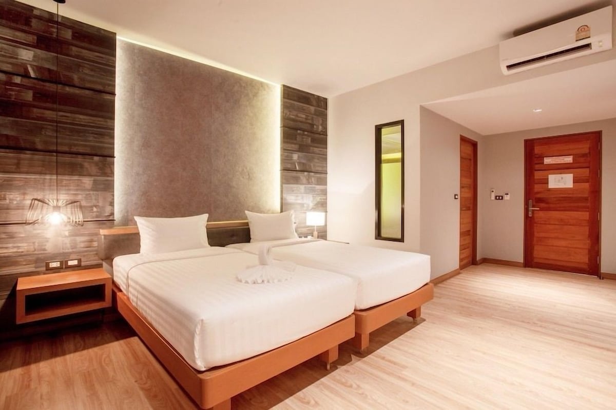 Ein Hotelzimmer mit zwei Betten, Holzboden, Wand mit strukturierter Wandverkleidung und Klimaanlage.