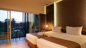 A hotel room with two beds, a balcony with a table and chairs, and a view of palm trees.