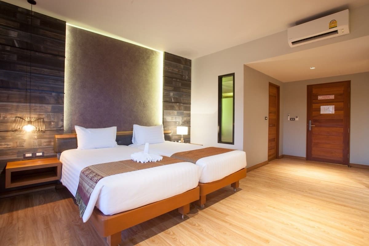 Une chambre d’hôtel moderne avec un grand lit, deux tables de chevet, un climatiseur fixé au mur et un plancher en bois.