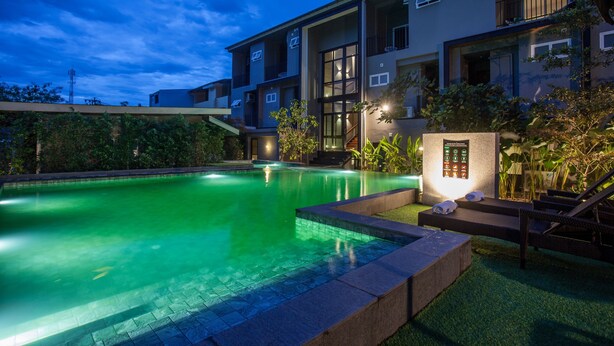 A modern building with a swimming pool, outdoor seating, and a well-lit entrance.