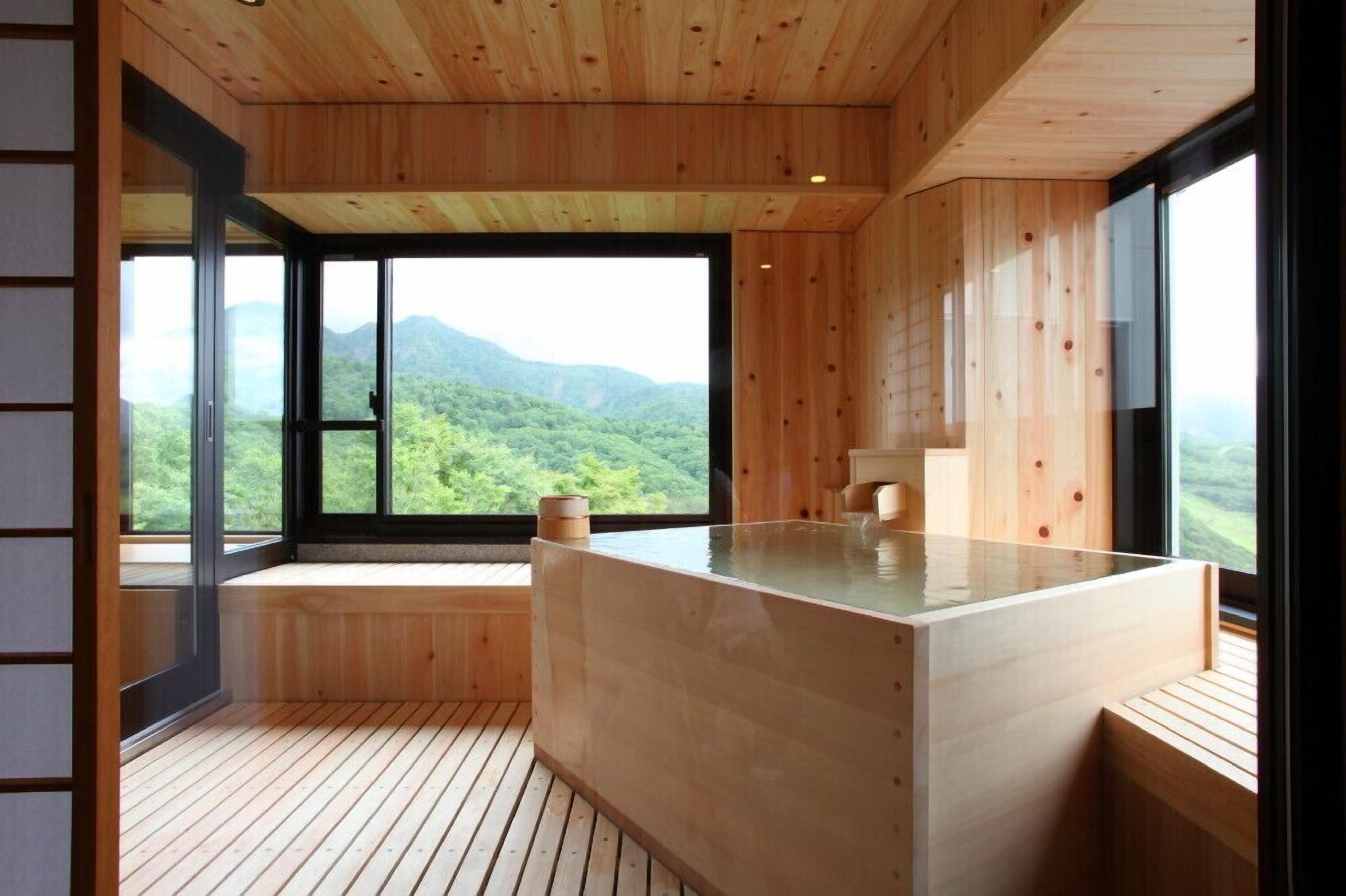 A wooden interior with a hot tub, large windows, and a view of a forested mountain.