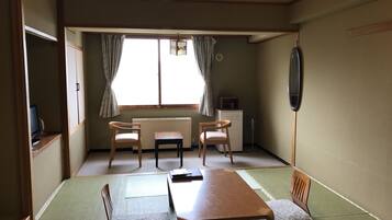 A traditional Japanese room with tatami flooring, a low table, two chairs, a small heater, and a television.