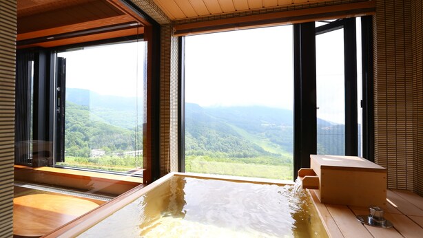 Ein Whirlpool mit Holzvertäfelung und Blick auf eine gebirgige Landschaft durch große Fenster.