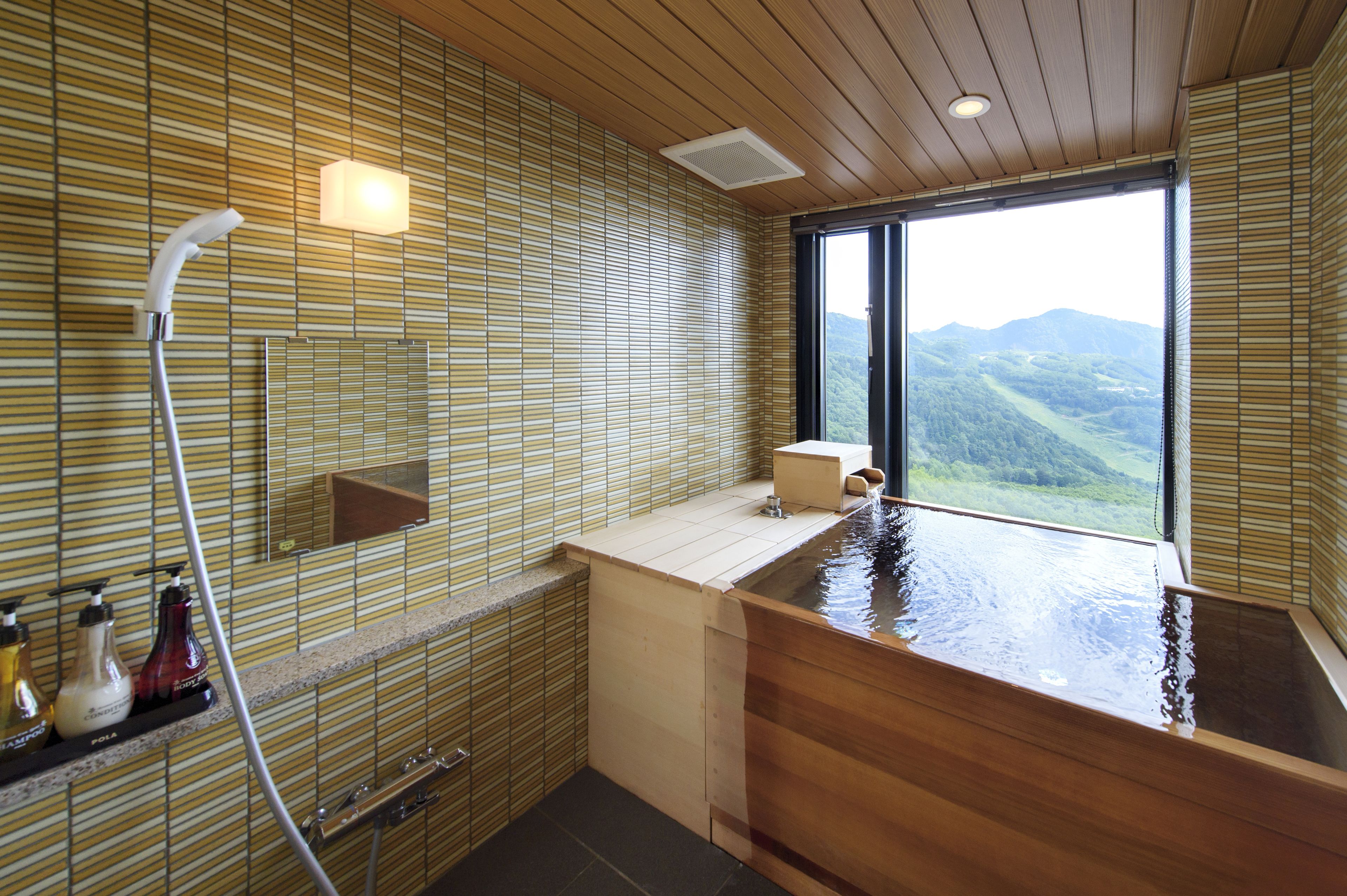 A modern bathroom with a wooden bathtub, a large window offering a view of the mountains, and a shower area with a glass enclosure.