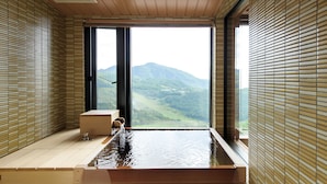 Ein moderner Wellnessraum mit Holzboden, einer großen Badewanne und Blick auf eine Berglandschaft durch große Fenster.