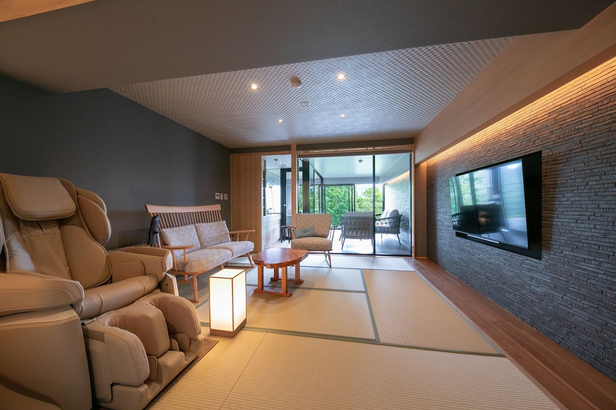 Un salón moderno con sillón de masaje, sofá y esterillas de tatami.