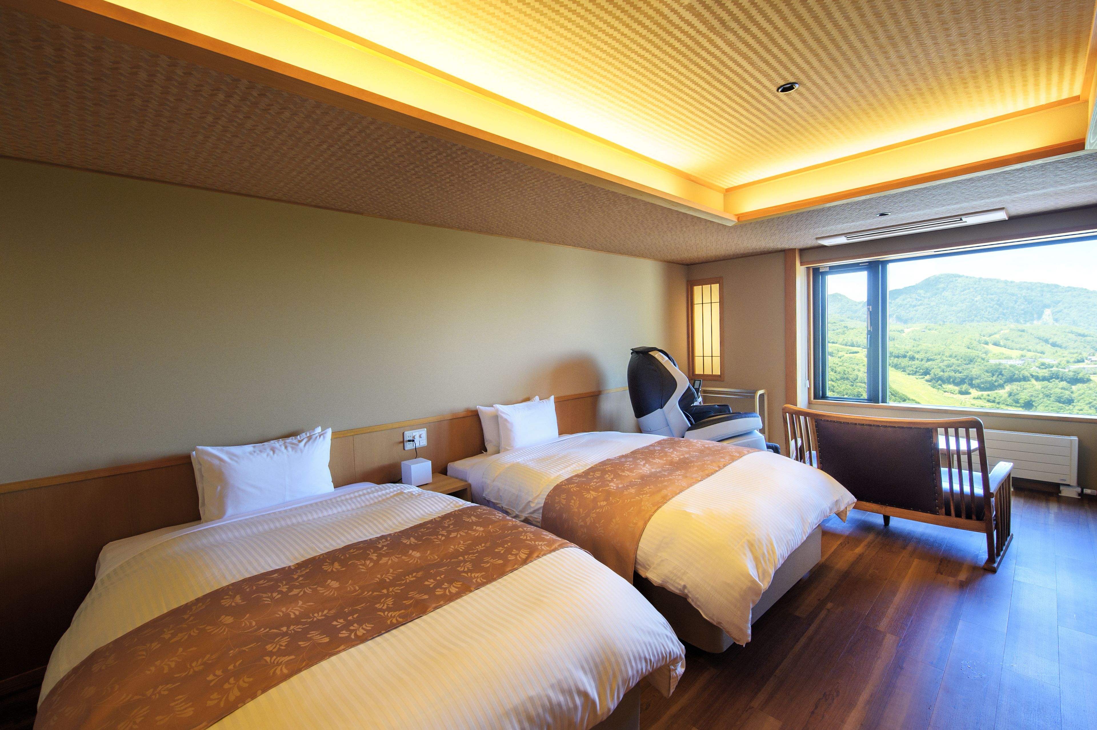 Habitación de hotel con dos camas, un escritorio y vistas a un paisaje montañoso.
