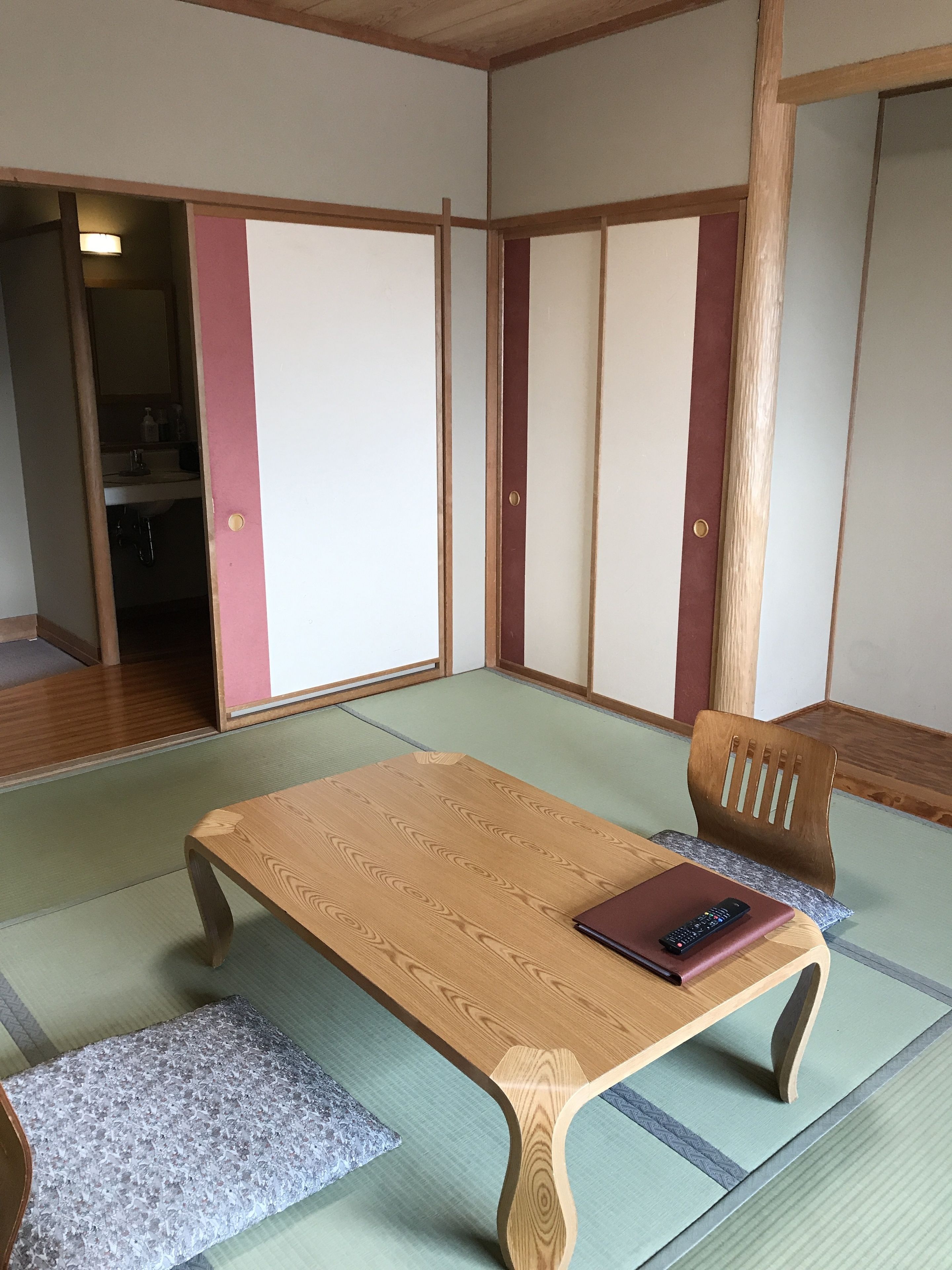 Una habitación japonesa tradicional con suelo de tatami, una mesa de madera baja, un banco acolchado y puertas correderas.