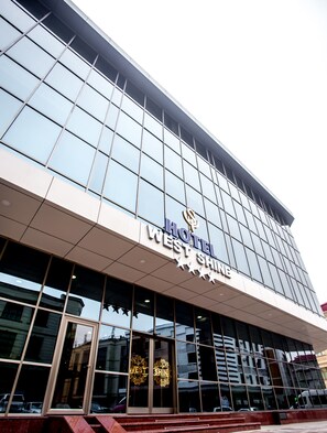A modern hotel building with a large glass facade and a prominent sign reading "HOTEL WEST SHINE".