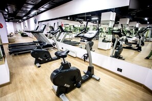 A gym with multiple exercise machines, including treadmills and stationary bikes, and a large mirror reflecting the equipment.