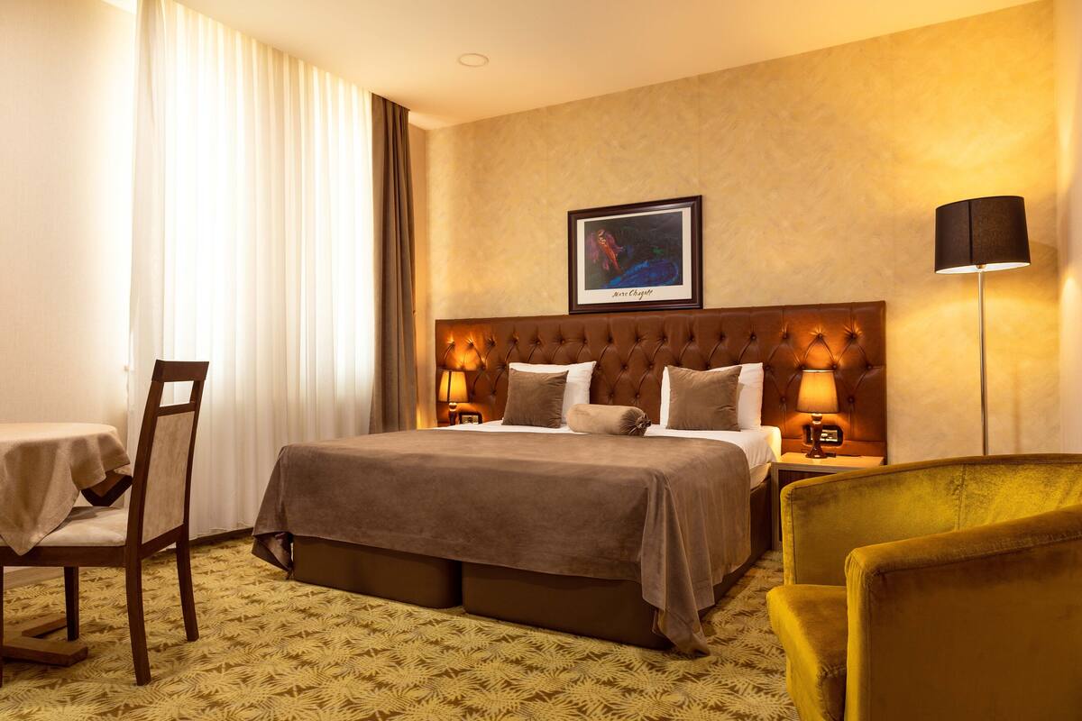 A hotel room with a large bed, two bedside tables, a chair, a desk, and a picture on the wall.