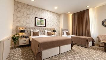 Habitación de hotel con una cama grande, una cama individual, una mesita de noche con lámpara, un aparador y un cuadro colgado en la pared.