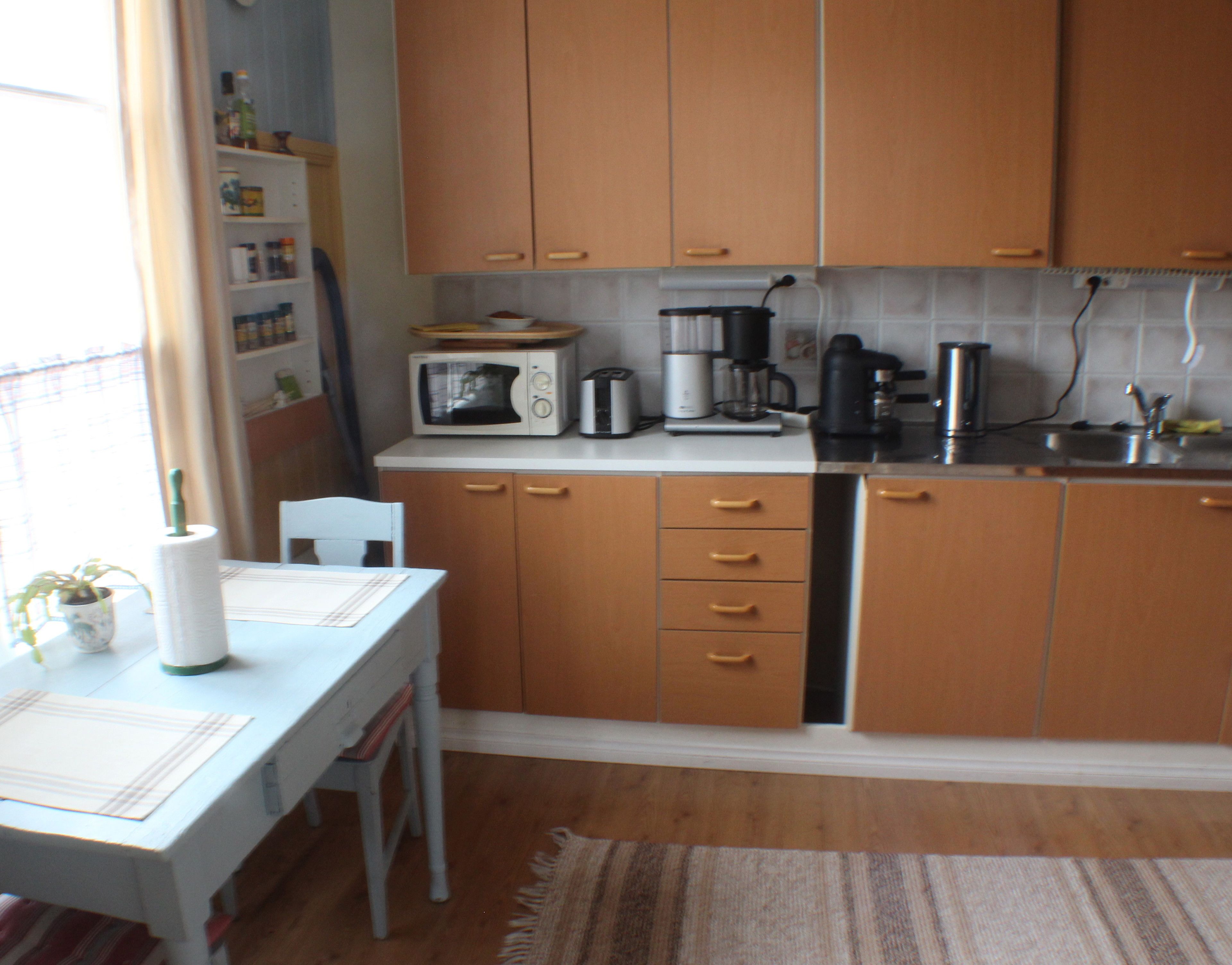 Una pequeña cocina con armarios de madera, microondas, cafetera y un lavamanos.