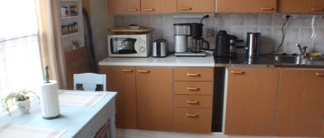 Una pequeña cocina con armarios de madera, microondas, cafetera y un lavamanos.