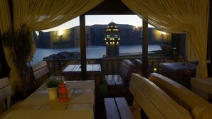 A dining area with wooden benches and tables, a view of a water body and a tower in the background.