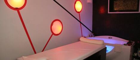 A spa room with a massage table, a small tub, and two wall-mounted light fixtures.