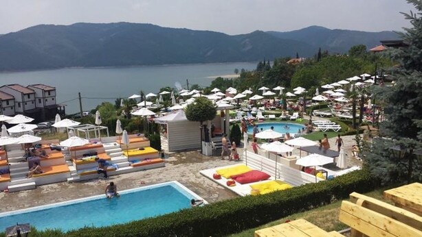 A resort with a swimming pool, sun loungers, umbrellas, and a view of the mountains.