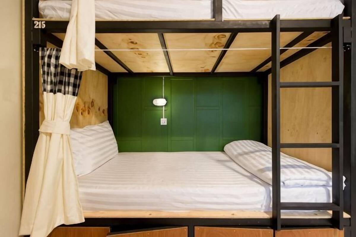 A bunk bed with a green headboard, a white curtain, and a small hanging light fixture.