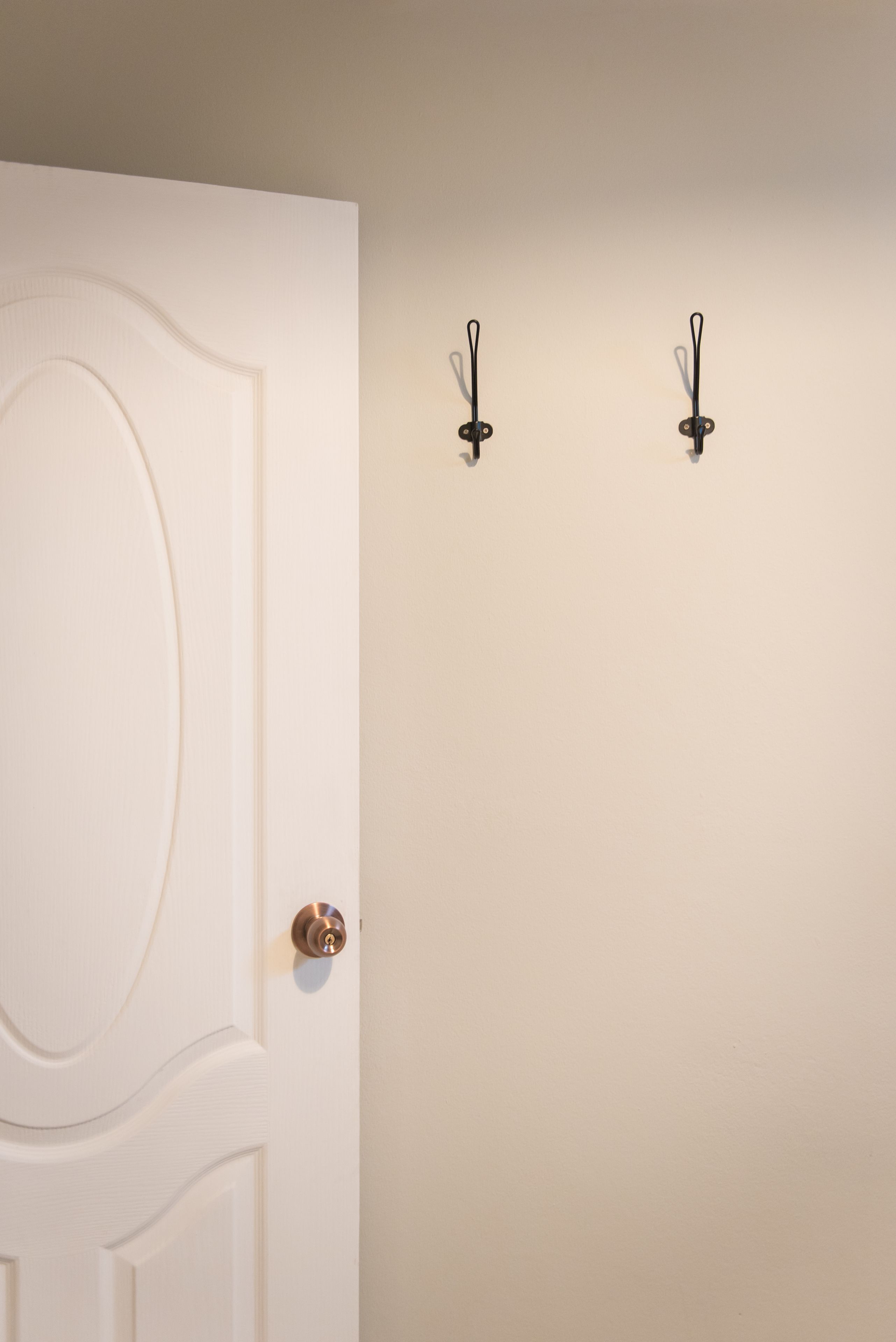 A white door with a brass doorknob and two wall-mounted hooks.
