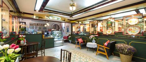 A restaurant interior with a wooden dining table, chairs, a patterned rug, and a display of plates on the wall.