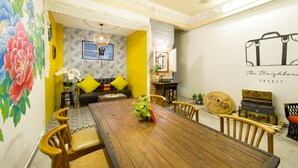 A dining area with a wooden table, chairs, and a decorative wall with a suitcase illustration. - The Neighbors Hostel - Adults Only (Phuket)
