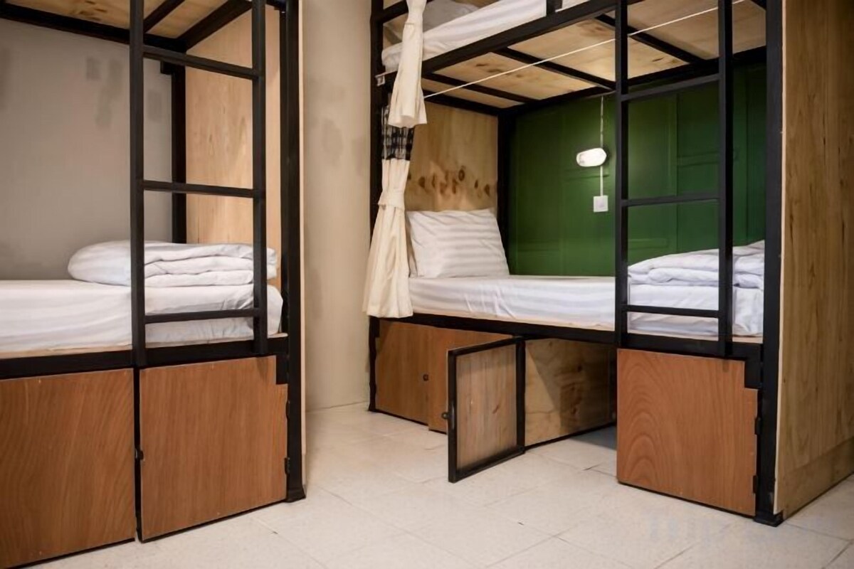 Una habitación con dos literas, piso de madera y pared verde.