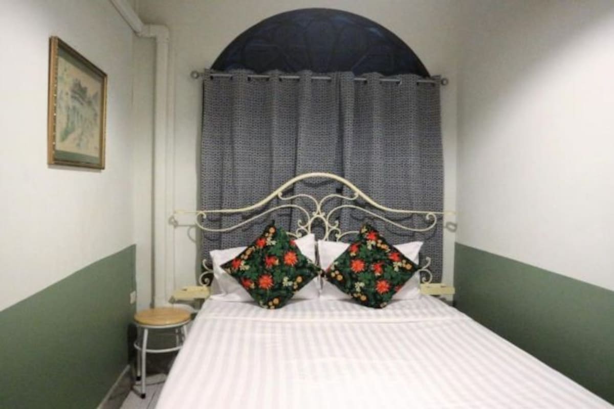 Una habitación con una cama, un taburete pequeño y un cuadro en la pared.
