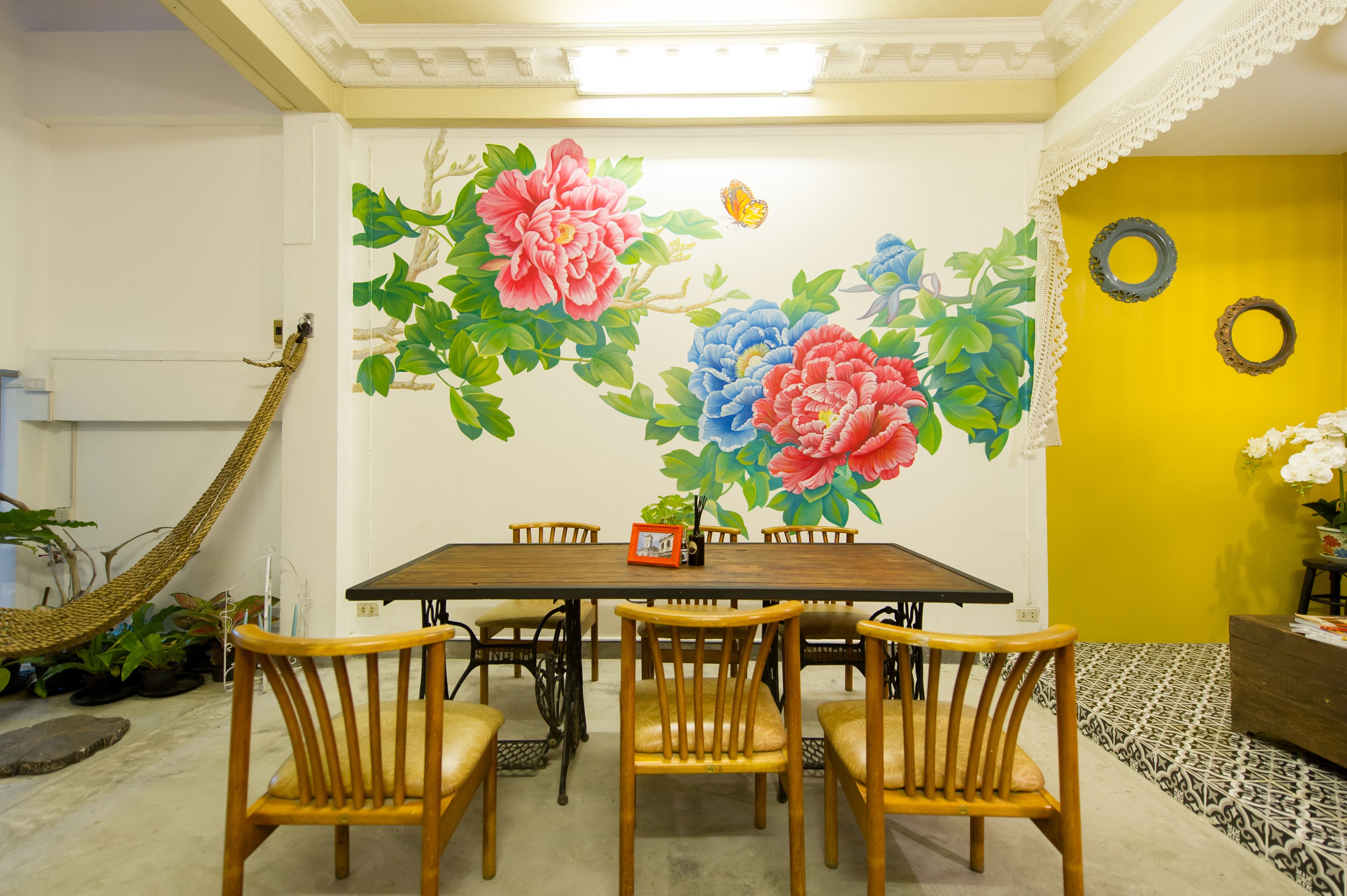 Comedor con una mesa dispuesta para seis personas, rodeada de sillas de madera. Un gran mural floral decora la pared detrás de la mesa.
