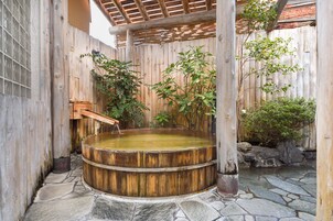 Un baño de aguas termales de madera con suelo de piedra, rodeado de paredes de madera y plantas.